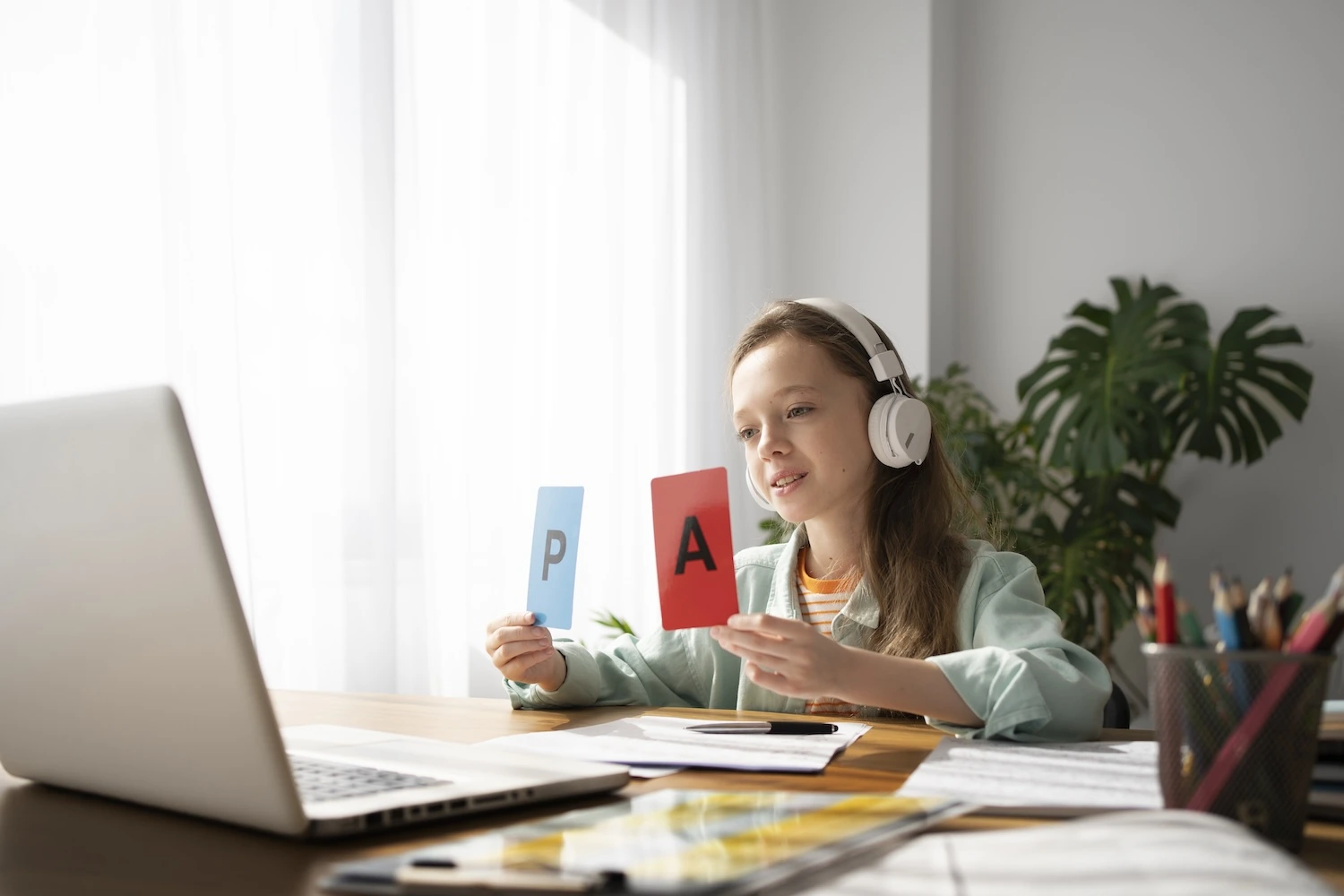 A girl lerning online holding alphabet cards